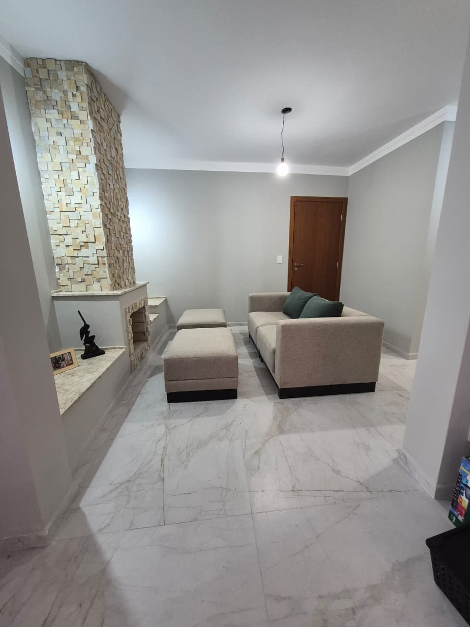 Sofá bege e pufes em sala com lareira de pedra